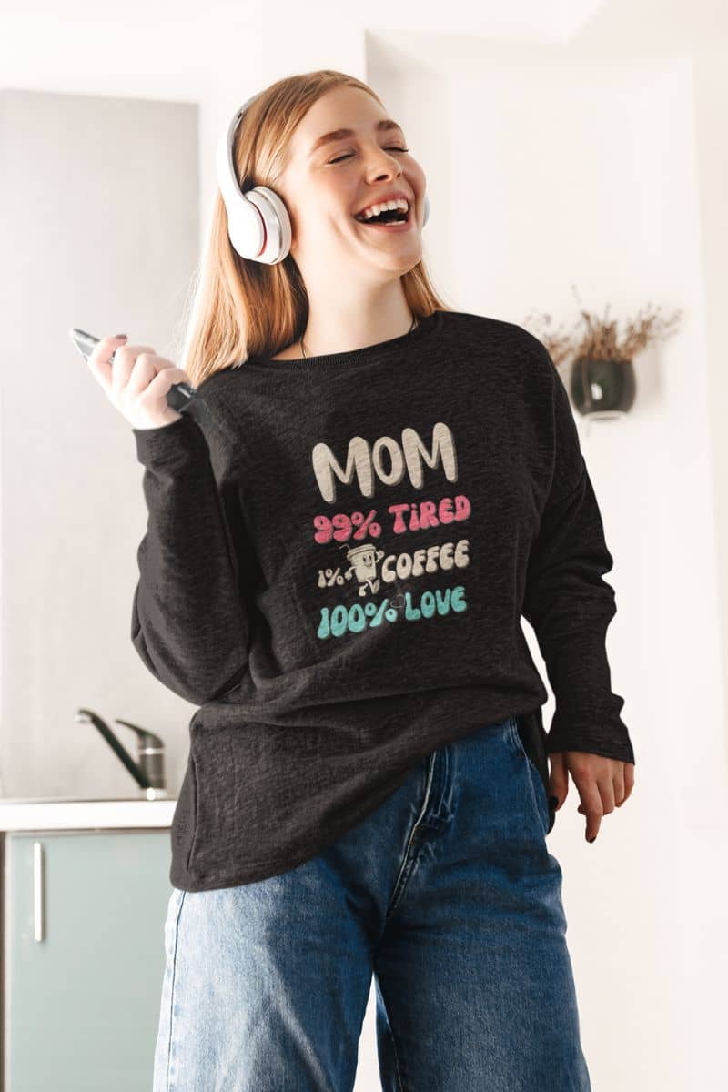 tired mom sweatshirt with a person wearing a sweatshirt with text 'Mom 99% Tired, 1% Coffee, 100% Love', laughing in a kitchen.
