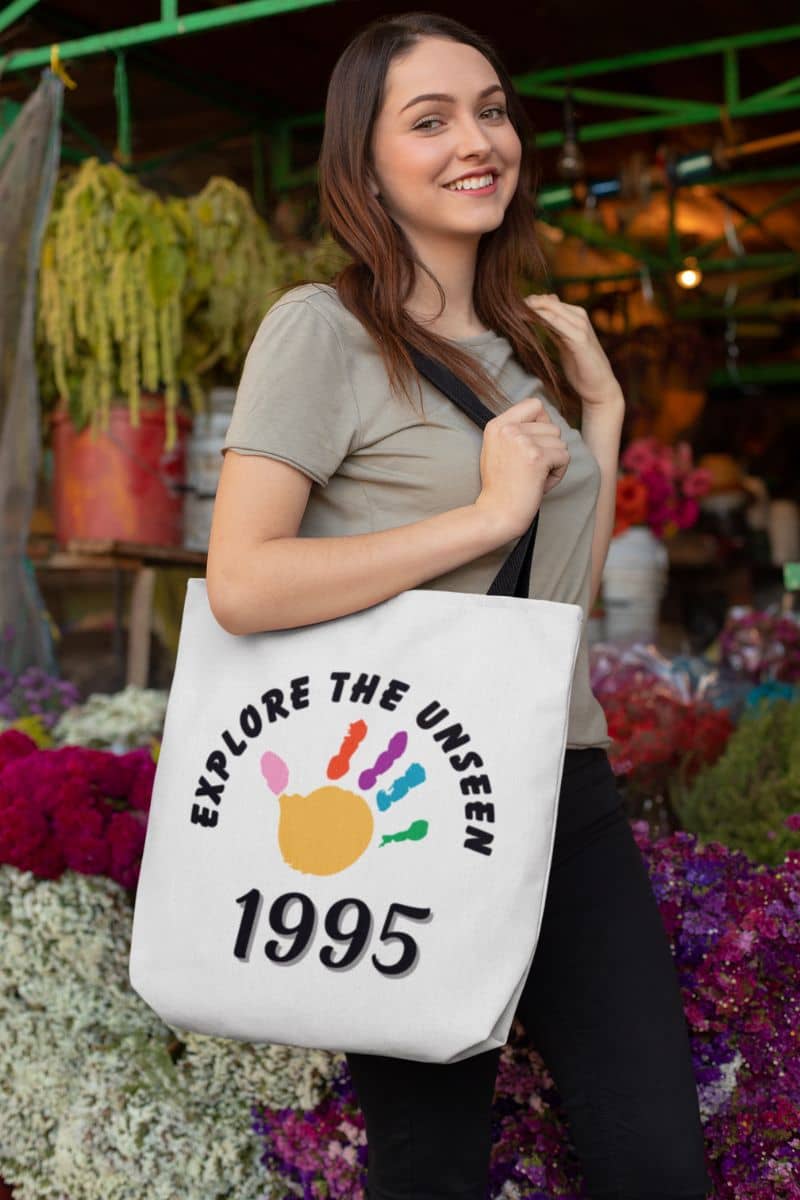 travel canvas tote bag with a woman holding a tote bag with 'Explore the Unseen 1995' design in a market setting.