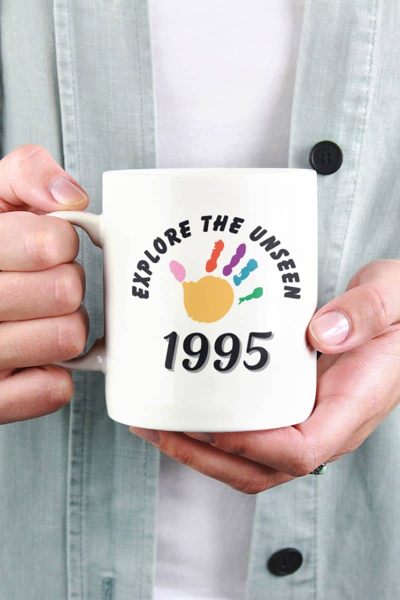travel gift coffee mug with a person holding a mug with 'Explore the Unseen 1995' text