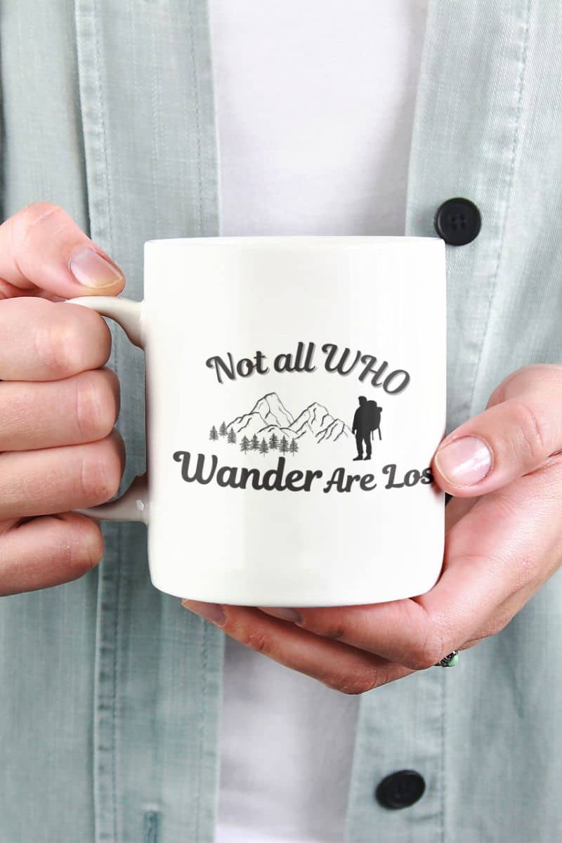 travel quote coffee mug with a person holding a mug with 'Not all who wander are lost' text and graphic