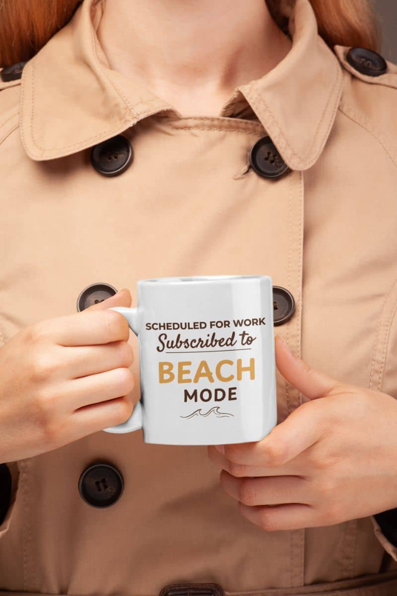 vacation coffee mug with a person holding a mug with text 'Scheduled for work, Subscribed to Beach Mode' against a beige coat background.