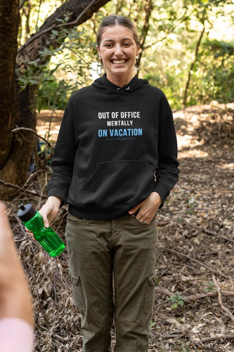 vacation mode hoodie with a person wearing a black hoodie with text 'Out of Office: Mentally on Vacation' in a forest setting