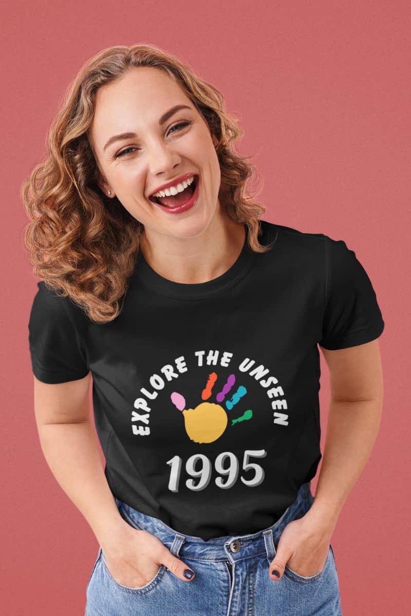 wanderlust t shirt with a woman wearing a black t-shirt with 'Explore the Unseen 1995' design on a pink background