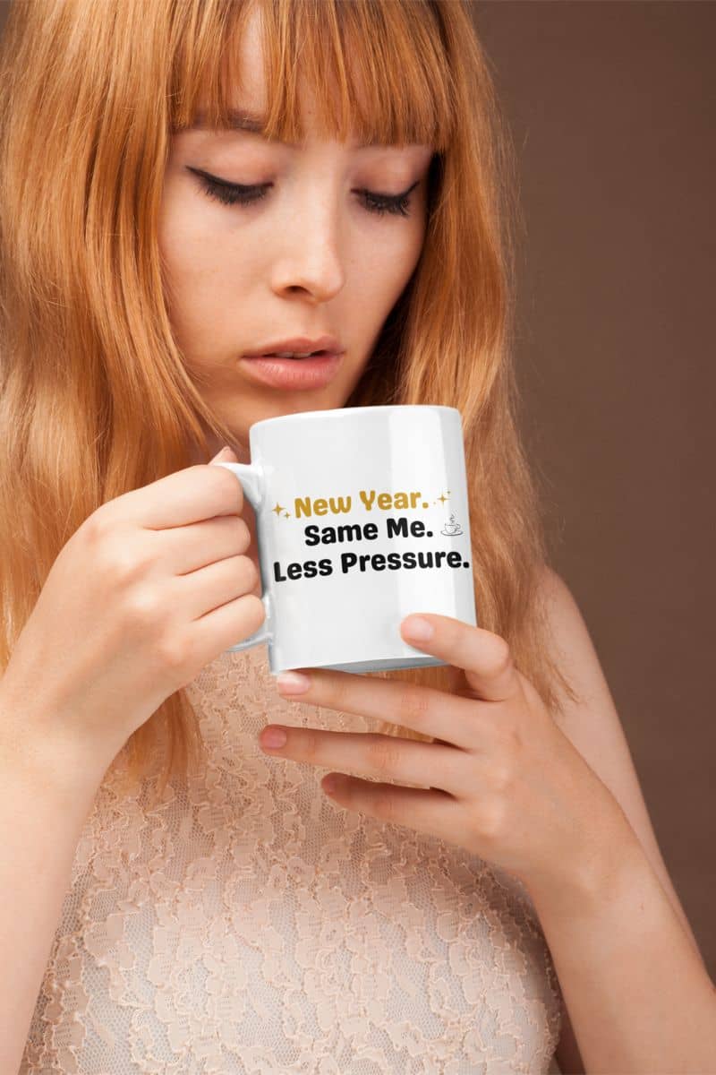 wellness quote mug with a woman holding a mug with humorous text 'New Year. Same Me. Less Pressure.' against a plain background