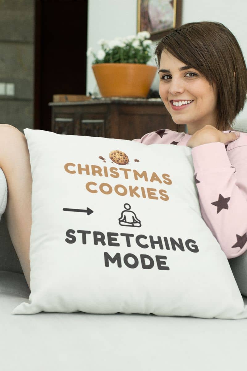 wellness quote pillow with a woman holding a pillow with text 'Christmas Cookies, Stretching Mode' in a home setting.