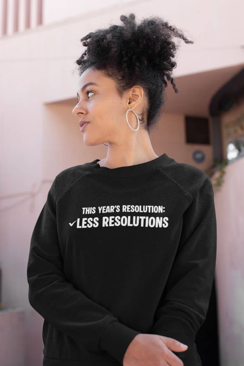 winter casual pullover with a person wearing a black sweatshirt with text 'This year’s resolution: Less resolutions.', standing outdoors.