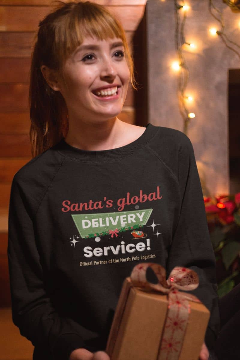 winter cozy pullover with a person wearing a black shirt with 'Santa's global delivery service' text, holding a gift box.