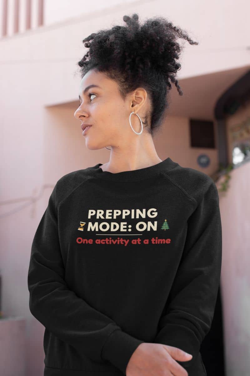 winter self care sweatshirt with a person wearing a black sweatshirt with text 'Prepping Mode: ON – One activity at a time', standing indoors.