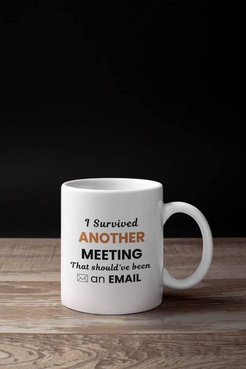 work coffee mug featuring a white mug with text 'I Survived Another Meeting That Should’ve Been an Email' on a wooden surface and black background