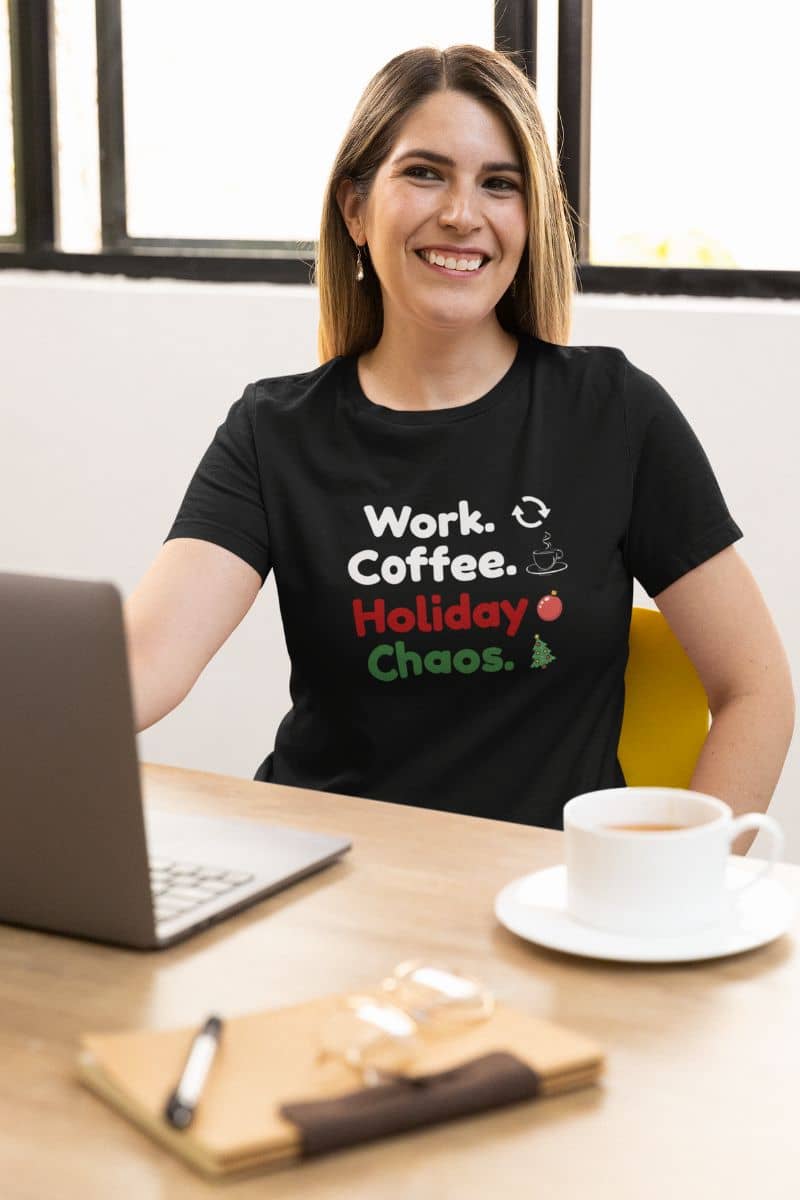 work from office christmas tee with a woman wearing a black t-shirt with  text 'Work. Coffee. Holiday Chaos.', sitting at a desk with a laptop and coffee.