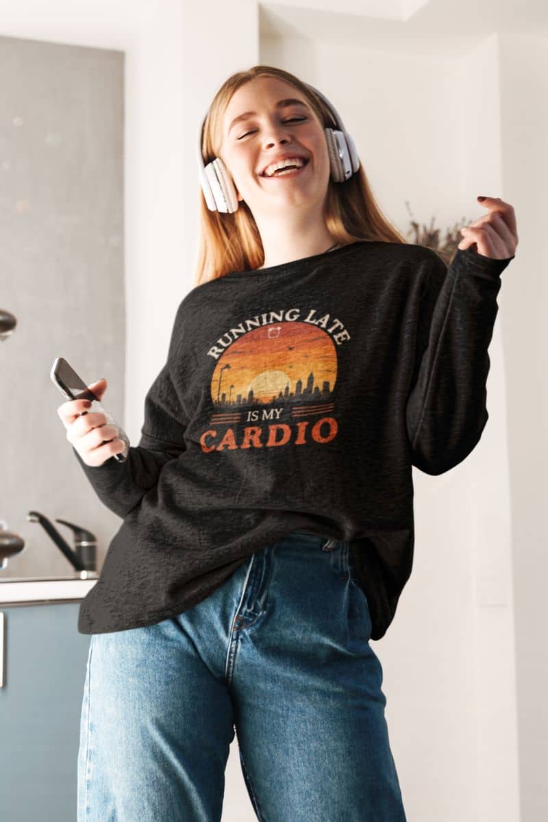work humor sweatshirt with a person wearing a black sweatshirt with a graphic design and text 'Running Late Is My Cardio', standing in a kitchen.