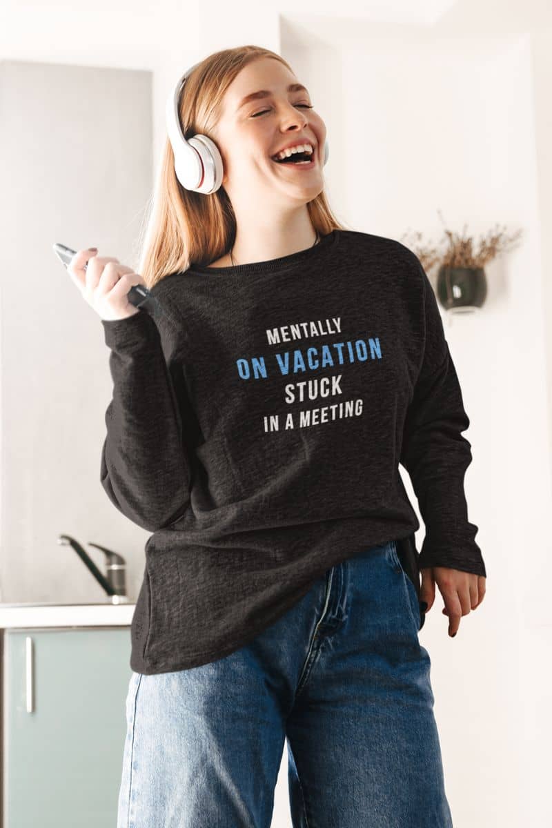 work humor sweatshirt with a person wearing a black sweatshirt featuring the text 'Mentally on Vacation. Stuck in A Meeting', laughing indoors.