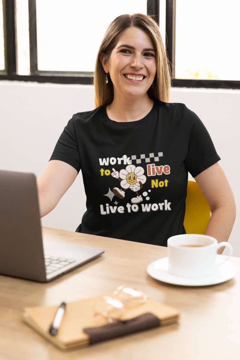 work-life balance t-shirt with a woman wearing a black t-shirt with a motivational quote 'Work to Live, Not Live to Work', sitting at a desk with a laptop and coffee.