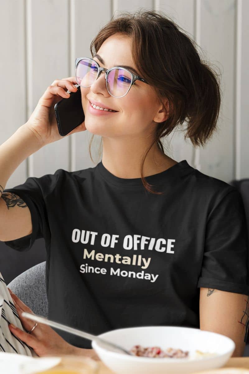 A person wearing a work sarcasm shirt featuring the text “Out of Office. Mentally Since Monday.” while talking on the phone.