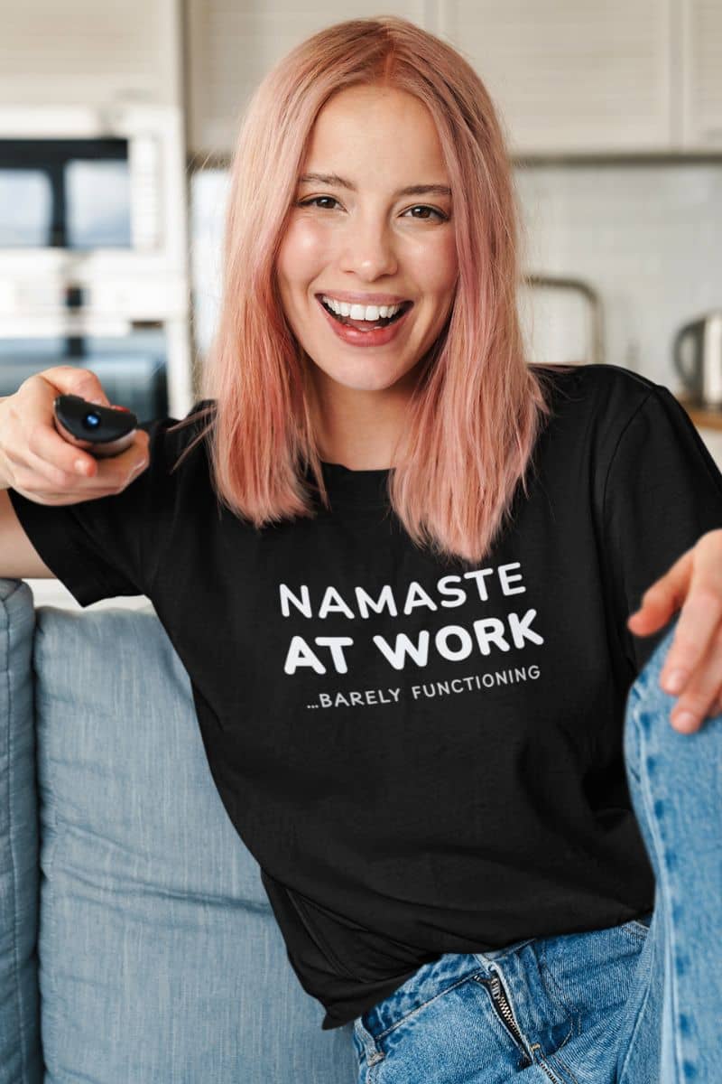 work stress shirt with a person wearing a black t-shirt with text 'Namaste at Work... Barely Functioning', sitting on a couch.