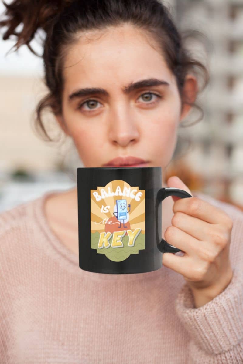 work life balance mug with a person holding a black mug with a colorful design and text.