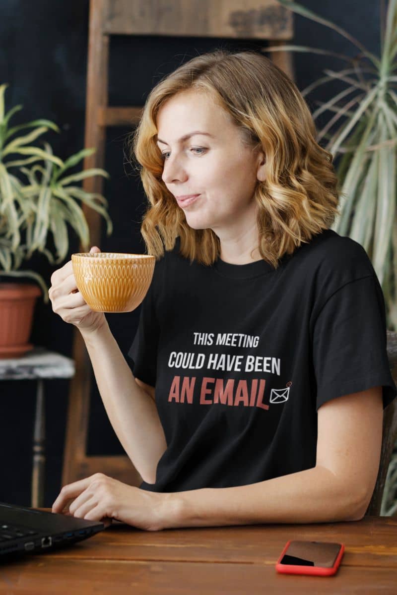 workplace humor shirt with a woman holding a cup with text 'This Meeting Could Have Been An Email' on her shirt in an indoor setting