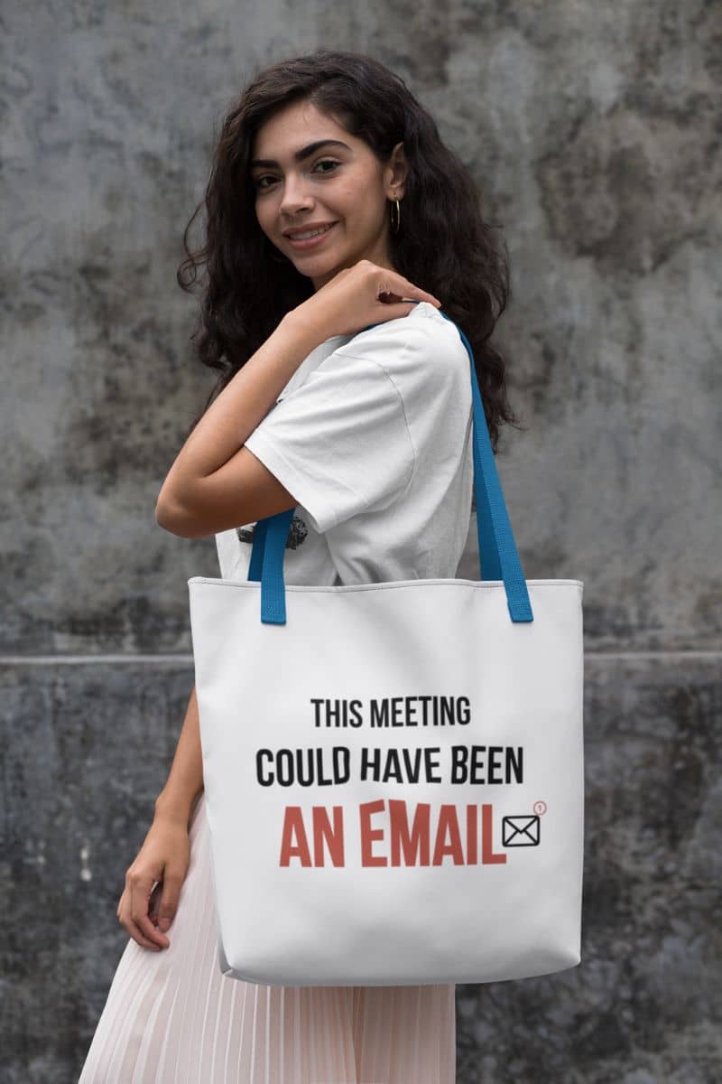 workplace humor tote with a woman holding a tote bag with text 'This meeting could have been an email' against a textured wall.