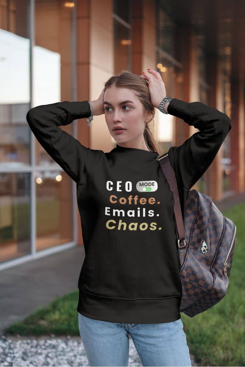 A workplace quote sweater with a woman in a black sweatshirt with text 'CEO Mode: Coffee. Emails. Chaos.'