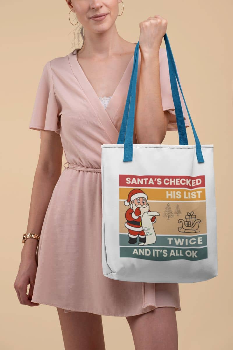xmas shopping tote with a woman holding a tote bag with text 'Santa's Checked His List Twice And It's All Ok' on a beige background