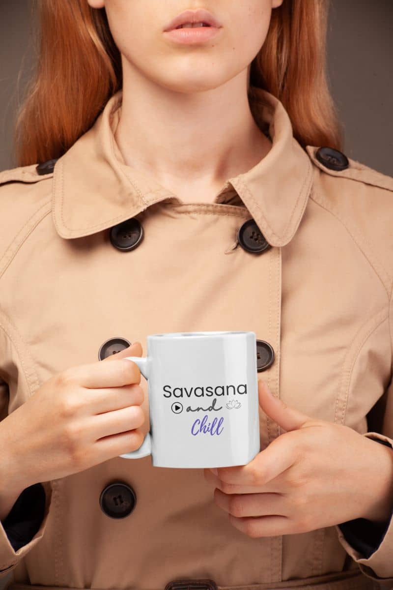 yoga gift mug with a person holding a mug with 'Savasana and Chill' text, wearing a beige trench coat.