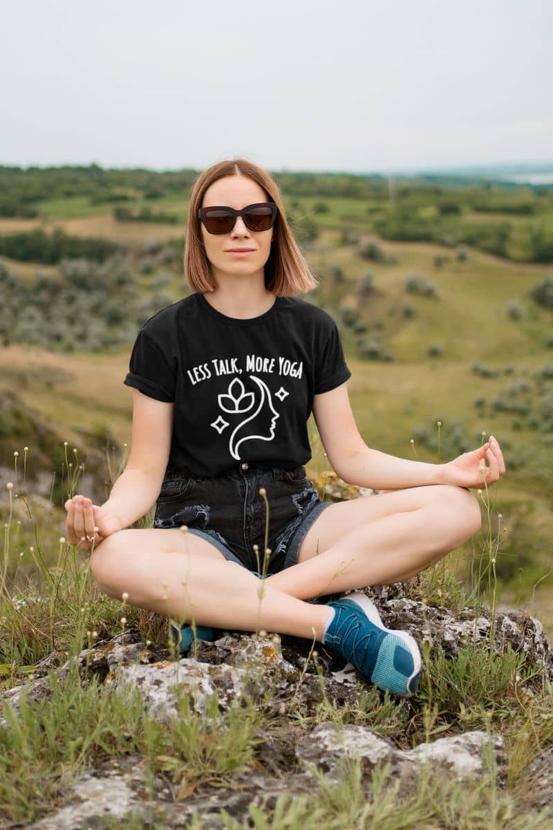 yoga humor shirt with a woman sitting outdoors in a field wearing a black t-shirt with text 'Less Talk, More Yoga '