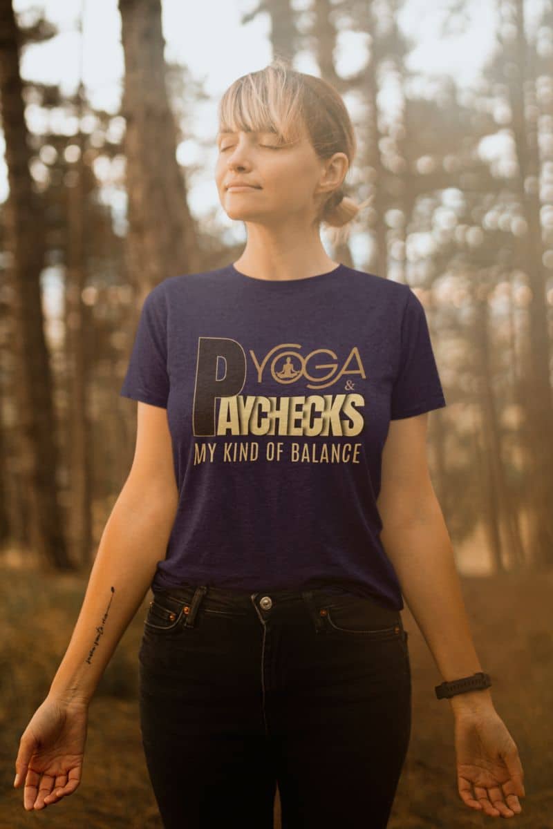 yoga lifestyle tee with a person wearing a purple t-shirt with text  'Yoga & Paychecks – My Kind of Balance.' in a forest setting