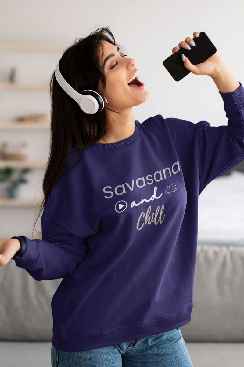 yoga pullover for women with a woman wearing a purple sweatshirt with 'Savasana and Chill' text, listening to music.