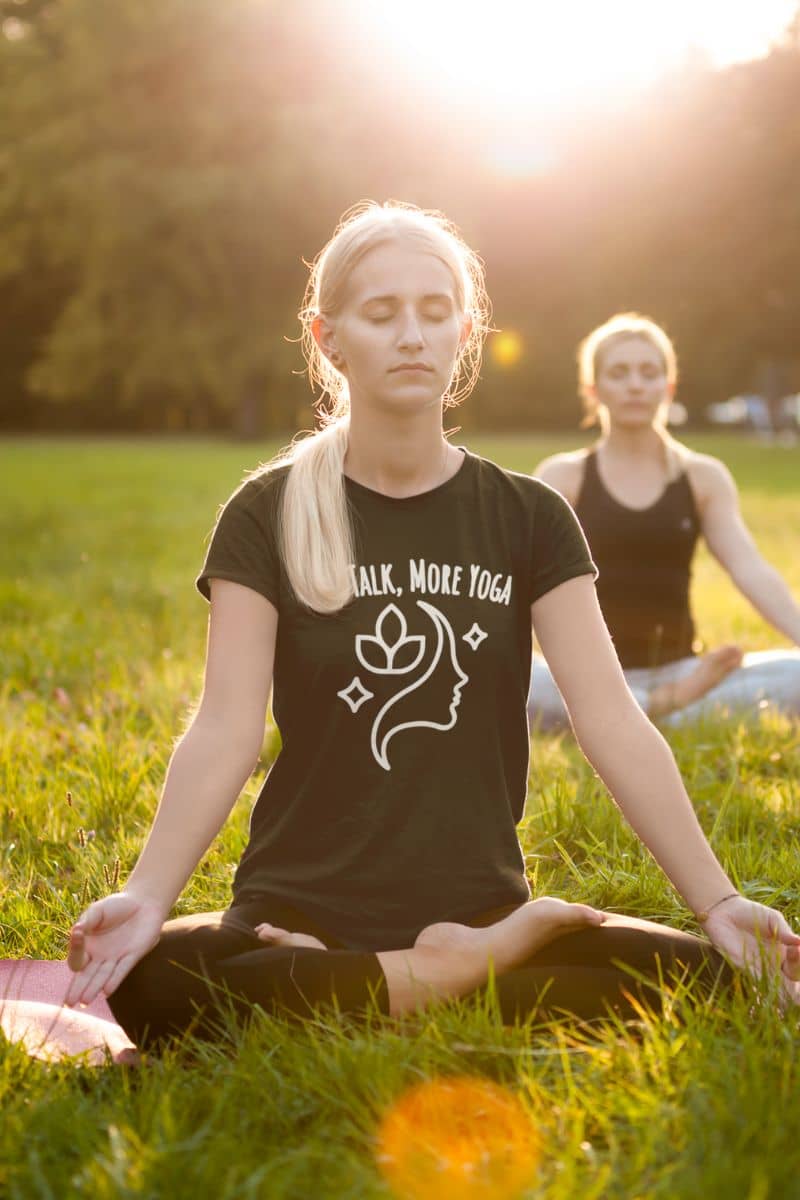 zen lifestyle apparel with a woman meditating in a park wearing a black t-shirt featuring the text 'Less Talk, More Yoga'